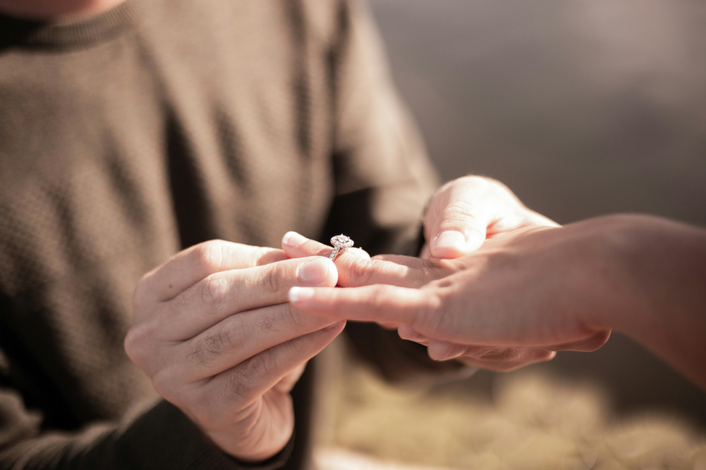 man in brown sweater putting an engagement ring on partner
